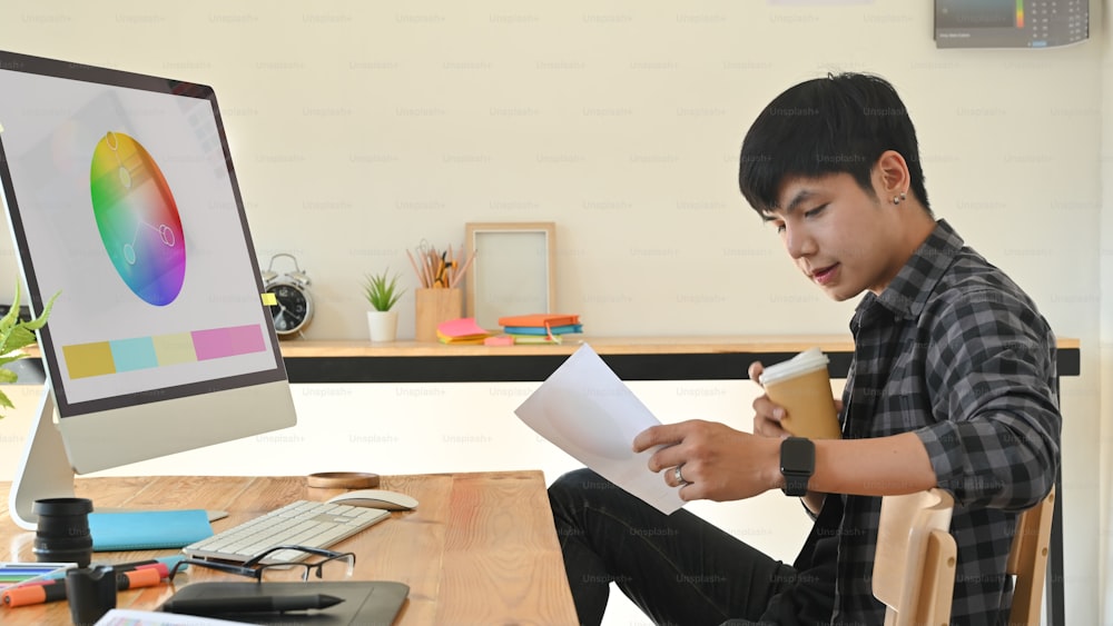 Homme créatif travaillant avec la couleur du papier et tenant une tasse de café sur le lieu de travail de la créativité.