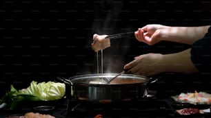 Plan recadré d’une femme mangeant du Shabu-Shabu dans une fondue avec de la viande fraîche tranchée trempée dans du fromage sur fond noir, cuisine japonaise