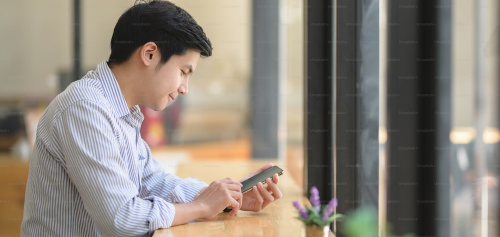 Porträt eines jungen Geschäftsmannes, der sein Smartphone am modernen Arbeitsplatz nutzt
