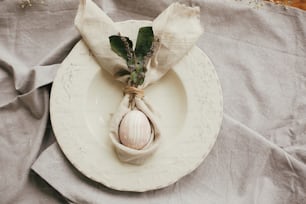 イースターバニーナプキンに卵が入ったスタイリッシュなイースターブランチテーブルセッティング。ウサギの耳が付いたナプキンにモダンな天然染めのピンクの卵、ヴィンテージプレートにラベンダーの花。イースターテーブルの装飾