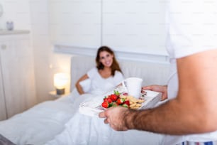 아침에 보살핌과 로맨스. 놀랐고 행복한 젊은 여자가 아침 식사를 가져오는 남성 손으로 침대에 누워 있다. 안녕하세요! 침대에서 건강한 아침 식사.