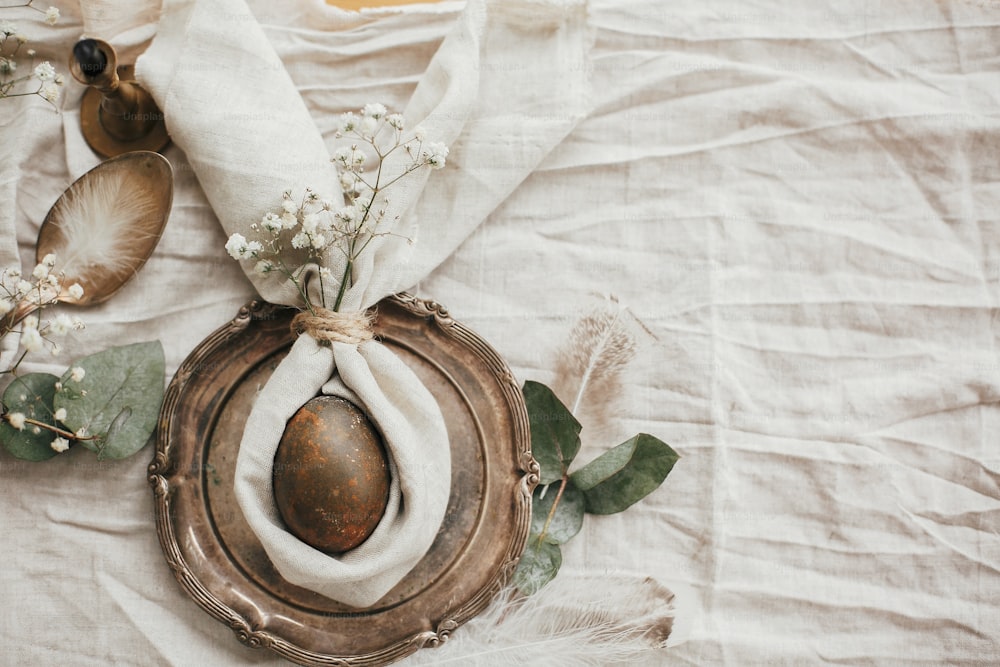 Stylish Easter brunch table setting with egg in easter bunny napkin. Modern natural dyed egg on napkin with bunny ears, flowers on vintage plate. Rustic Easter table decorations