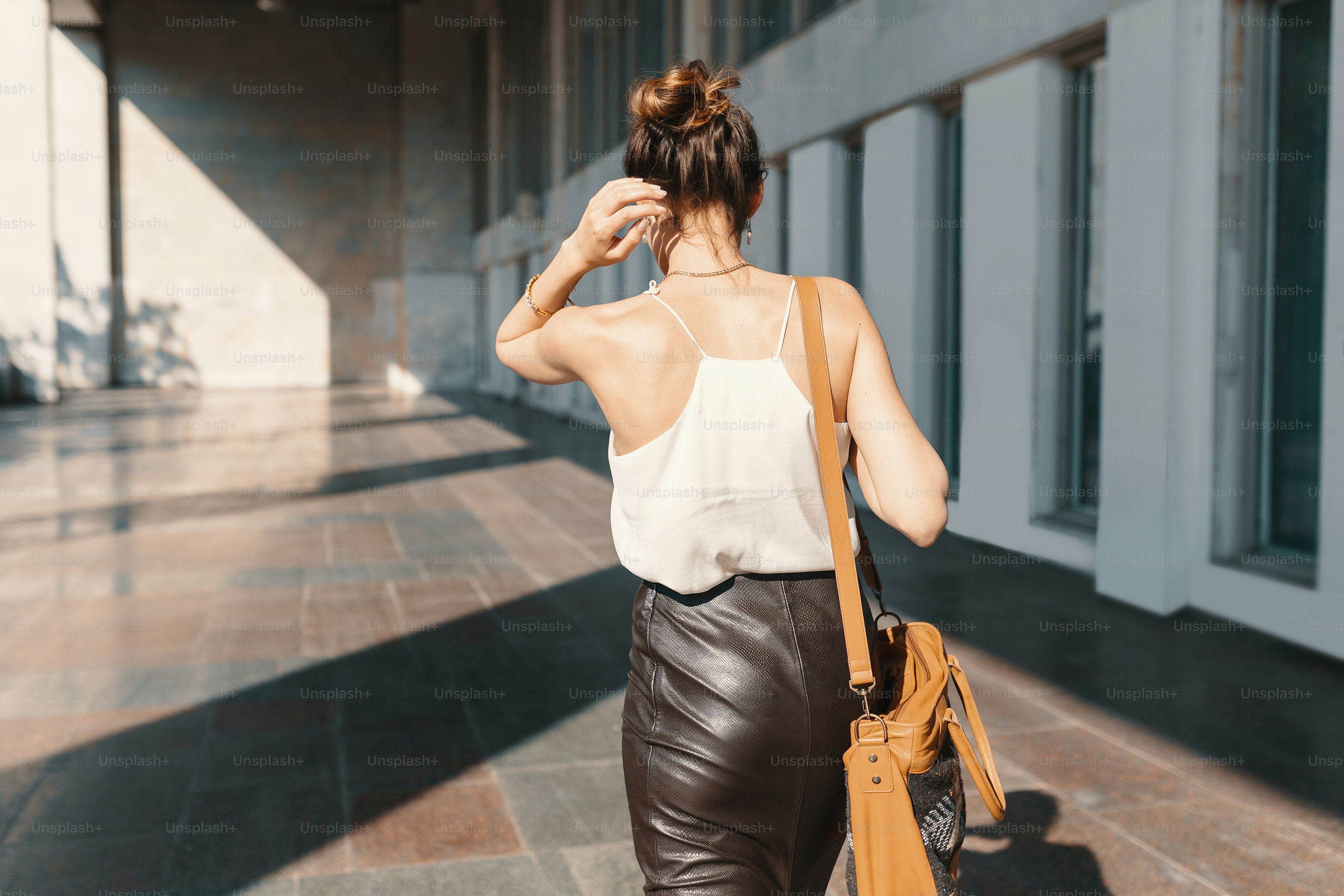 Business woman dressed in a leather pencil skirt, chiffon or silk blouse, wearing shoes with heels and sunglasses walking near a building