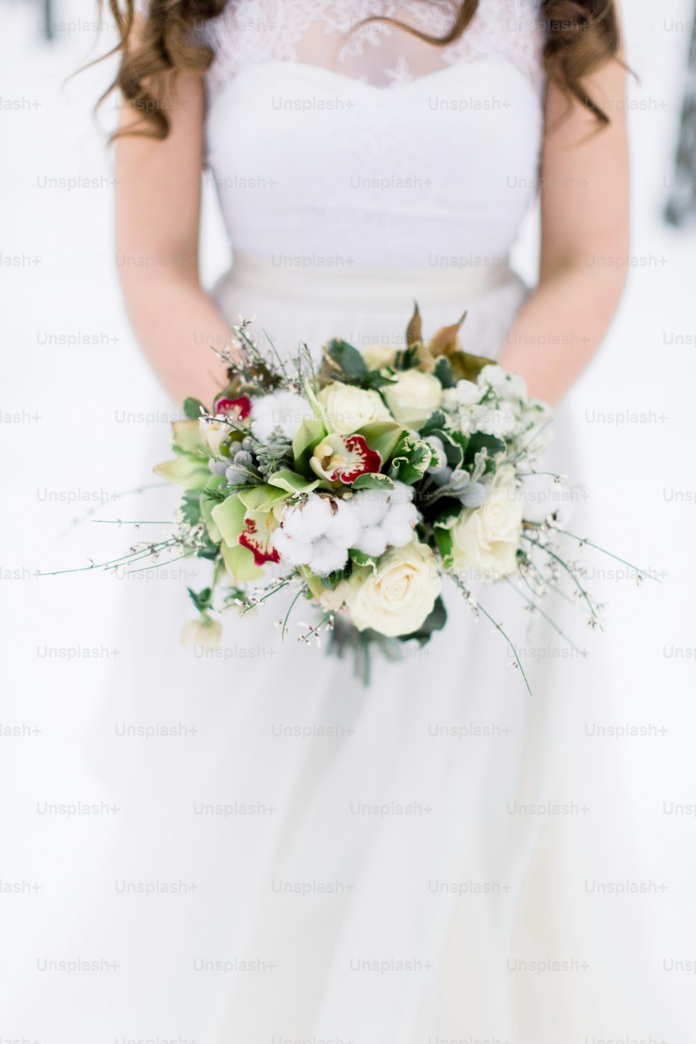 Wedding bouquet with flowers and cotton in hands of the bride. Winter time, snowy forest. Cropped image.