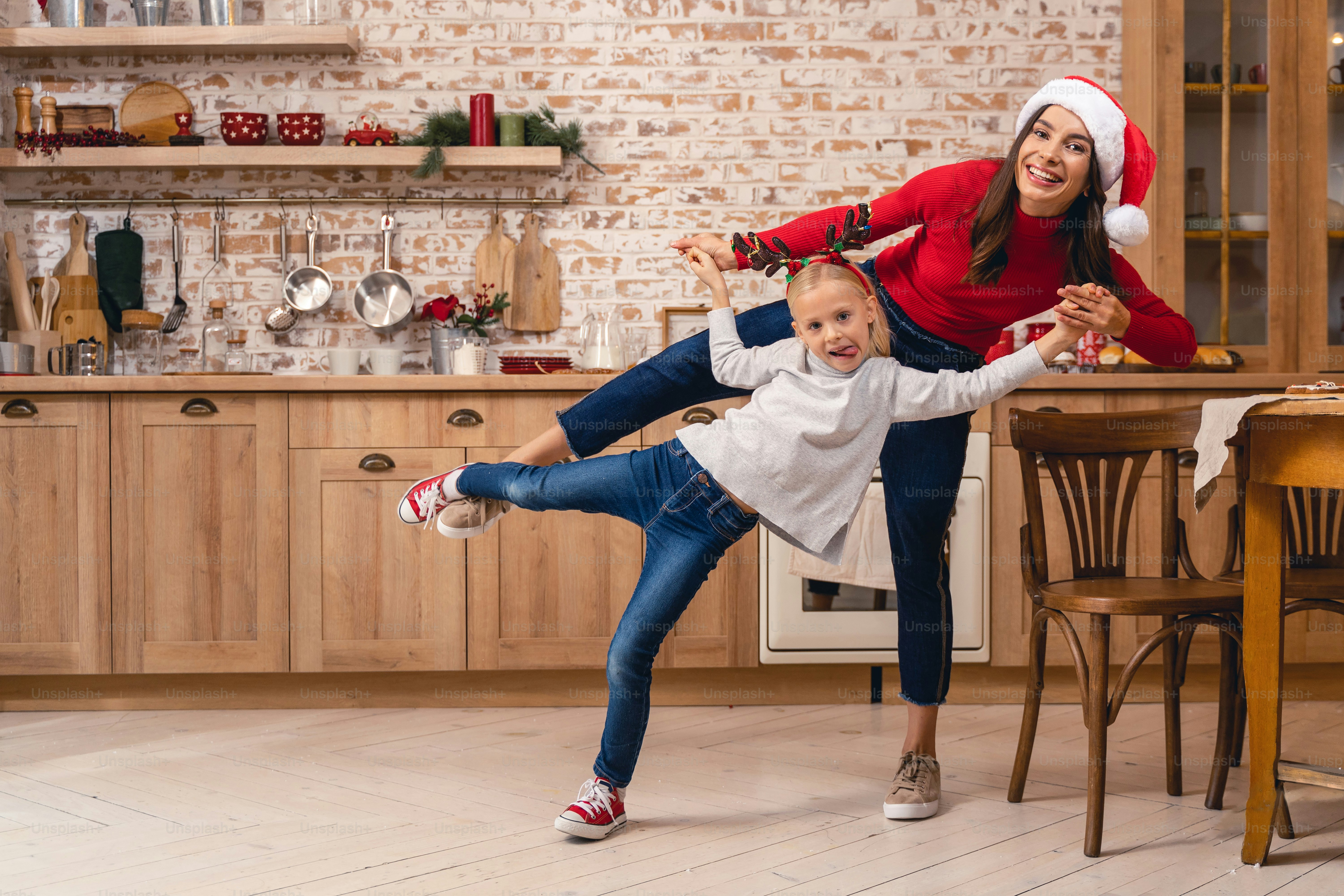 High-spirited mother and her daughter standing on one leg in the kitchen