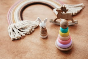 Eco friendly plastic free toys for toddler. Stylish wooden toys for child on wooden table. Modern colorful wooden pyramid with rings, wooden bunny and macrame rainbow.