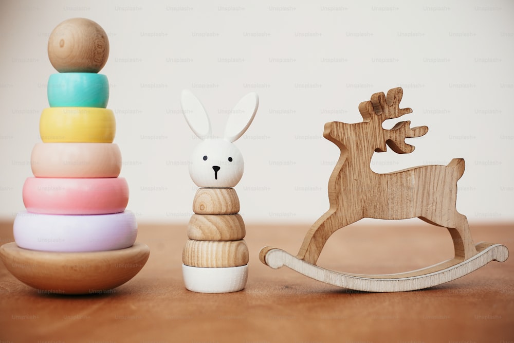 Stylish wooden toys for child on wooden table. Modern colorful wooden pyramid with rings, simple bunny and reindeer. Eco friendly plastic free educational toys for toddler