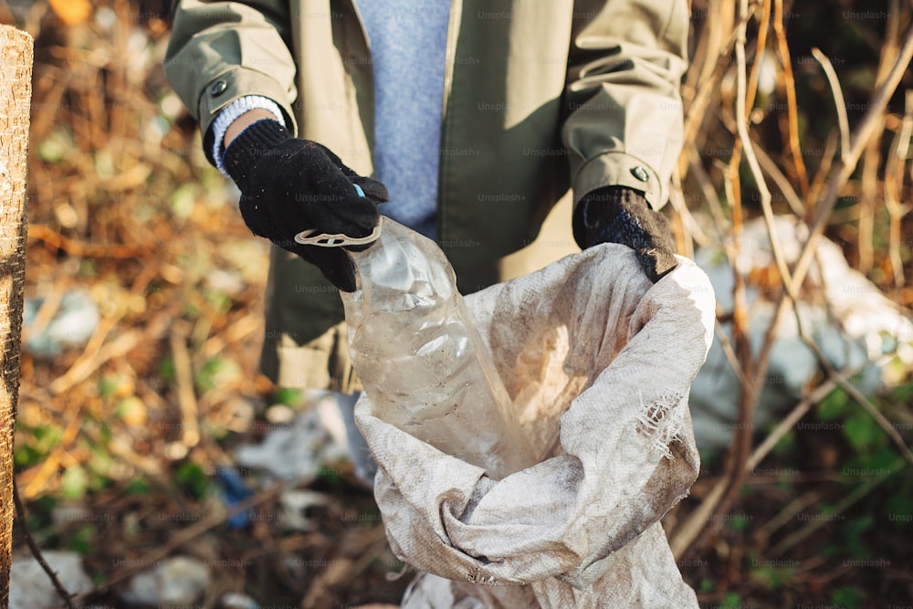 Eco ativista pegando garrafas plásticas sujas no parque. Mão da mulher na luva recolhendo o lixo, coletando o lixo no saco. Limpeza voluntária da natureza a partir de plástico de uso único