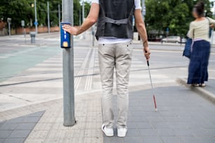 Sección media de un ciego con un bastón blanco en la señal de pitido del cruce de la pedestrina en la ciudad.