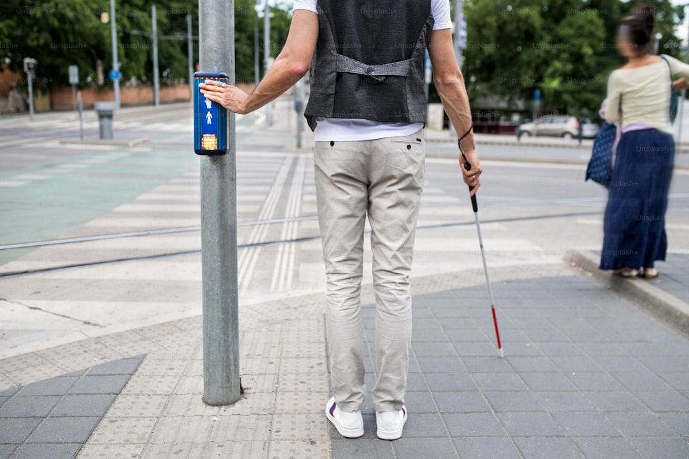Mittelteil des blinden Mannes mit weißem Stock am Pedestrain Kreuzung Piepsignal in der Stadt.