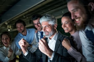 夕方、オフィスでコンピューターを手に、興奮を表現しているビジネスパーソンのグループ。