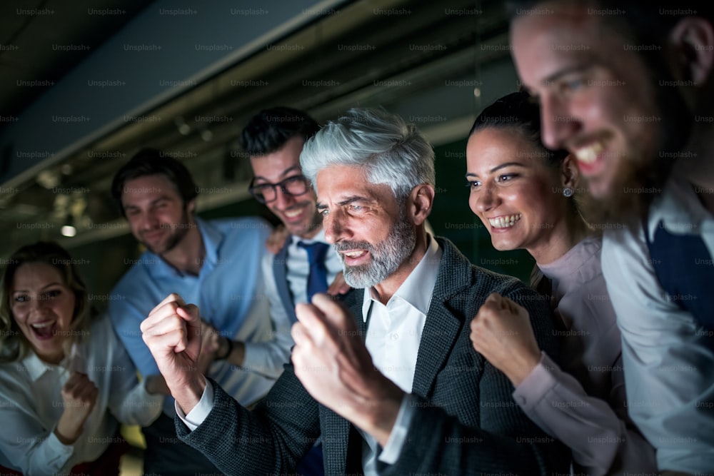Un gruppo di uomini d'affari con il computer in un ufficio la sera, esprimendo eccitazione.