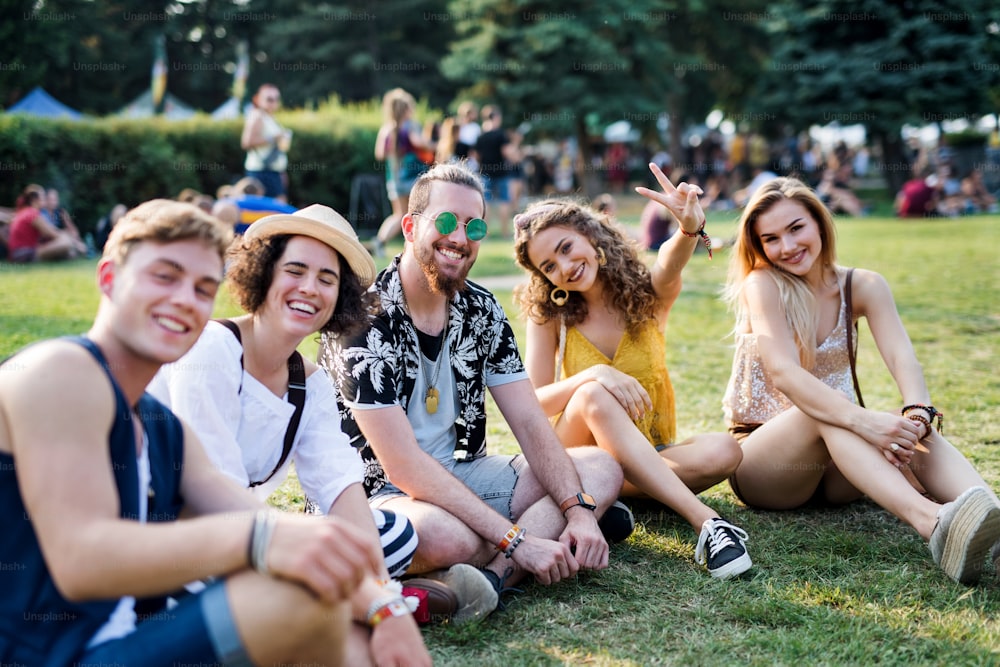 Eine Gruppe fröhlicher junger Freunde sitzt beim Sommerfest auf dem Boden und schaut in die Kamera.