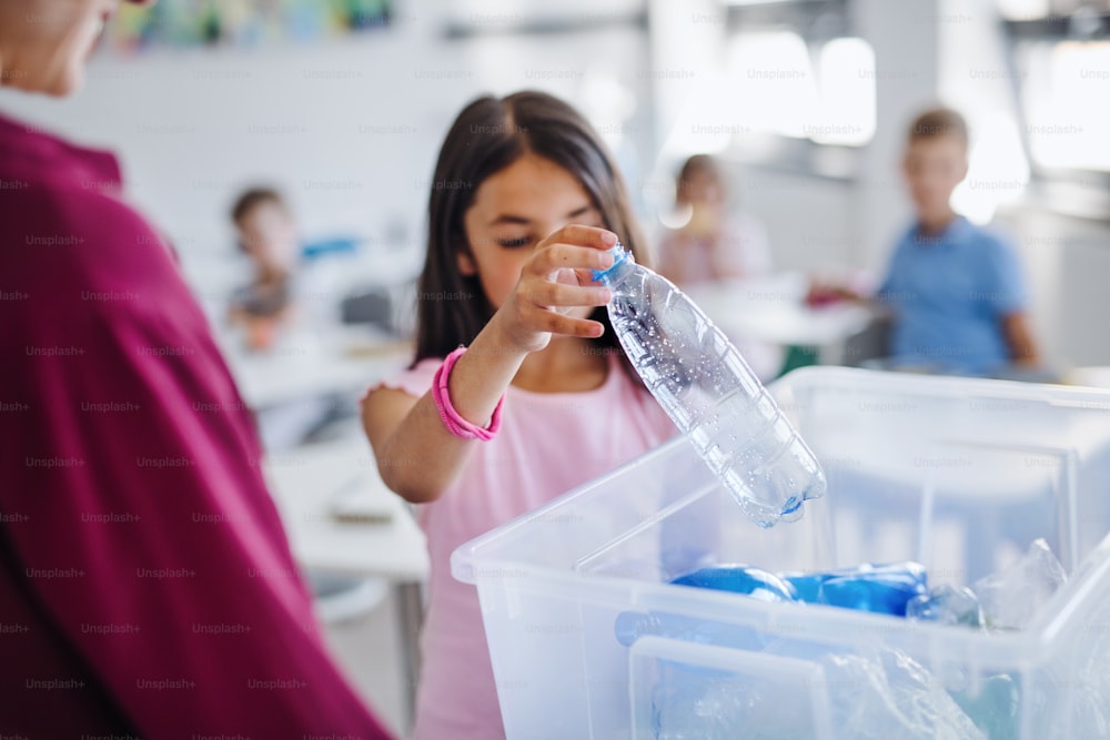 An unrecognizable teacher with small school kids in classroom learning about ecological waste separation.