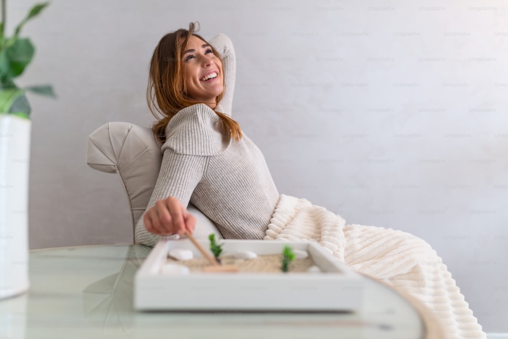 Portrait of beautiful young woman using her Zen garden at home. Lovely young smiling woman relaxing with her Zen garden and enjoying her day