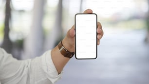 Cropped shot of young businessman showing his blank screen smartphone with blurred office background