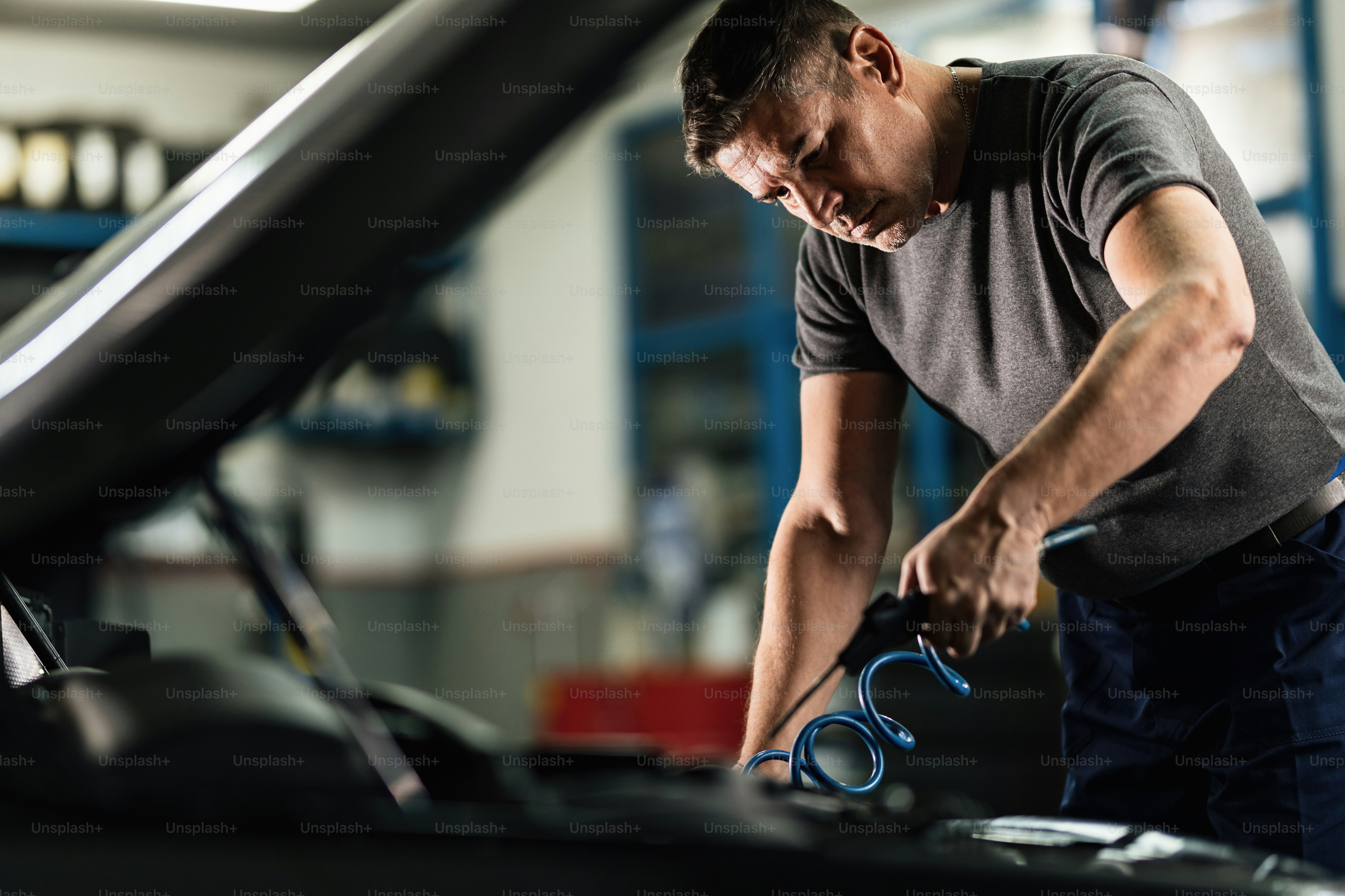 Auto mechanic using diagnostic tool while checking car battery voltage ...