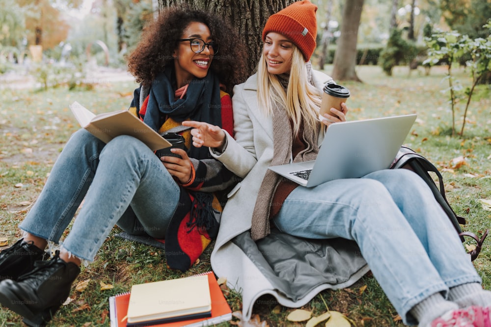 Happy ladies sitting near tree with book and coffee