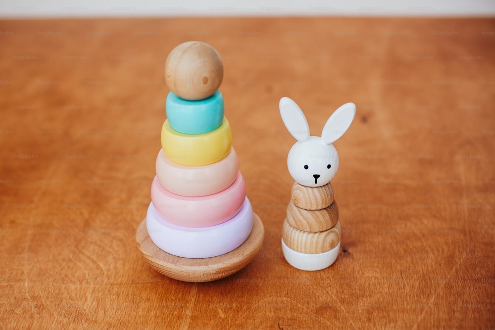 Stylish wooden toys for child on wooden table. Modern colorful wooden pyramid with rings and simple bunny. Eco friendly, plastic free educational toys for toddler