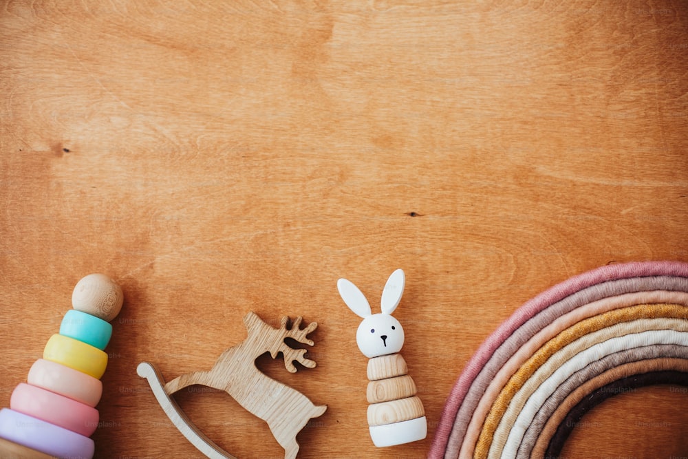 Eco friendly plastic free toys for toddler. Stylish wooden toys for child on wooden table. Modern colorful wooden pyramid with rings, wooden bunny and macrame rainbow. Flat lay