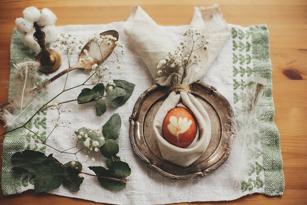 Stilvolle Osterbrunch-Tischdekoration mit Ei in Osterhasenserviette. Modernes naturgefärbtes Ei auf Serviette mit Hasenohren, Blumen auf Vintage-Teller. Rustikale Ostertischdekoration