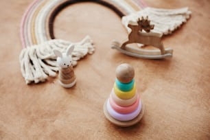 Stylish wooden toys for child on wooden table. Modern colorful wooden pyramid with rings, wooden bunny and macrame rainbow. Eco friendly plastic free toys for toddler