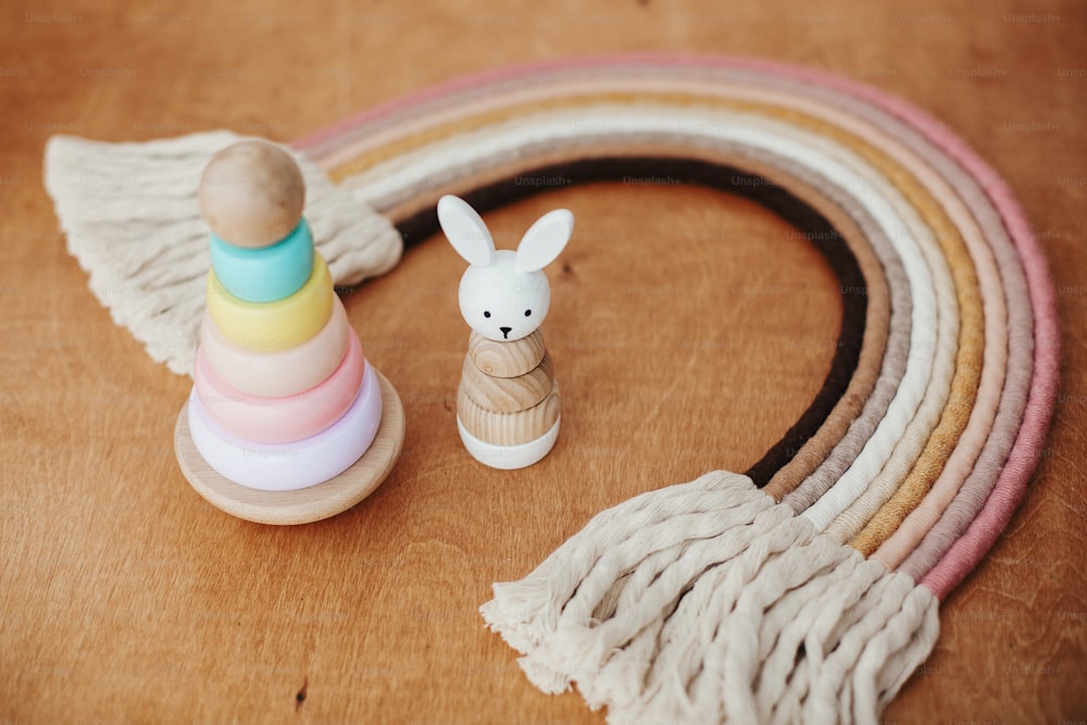 Stylish wooden toys for child on wooden table. Modern colorful wooden pyramid with rings, wooden bunny and macrame rainbow. Eco friendly plastic free toys for toddler