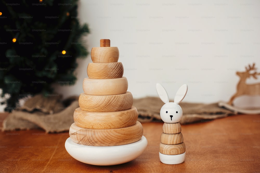 Stylish wooden toys for child on background of christmas tree. Modern simple wooden pyramid with rings and bunny. Eco friendly, plastic free educational toys for toddler