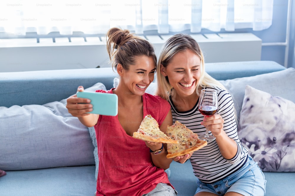 Amigos comendo pizza e sorrindo para selfie. Eles estão compartilhando pizza e fazendo selfie foto no telefone inteligente móvel. Eles estão fazendo festa em casa, comendo pizza e se divertindo.