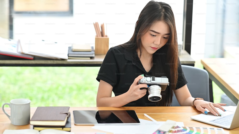Jeune femme créative travaillant avec un appareil photo et un ordinateur portable.