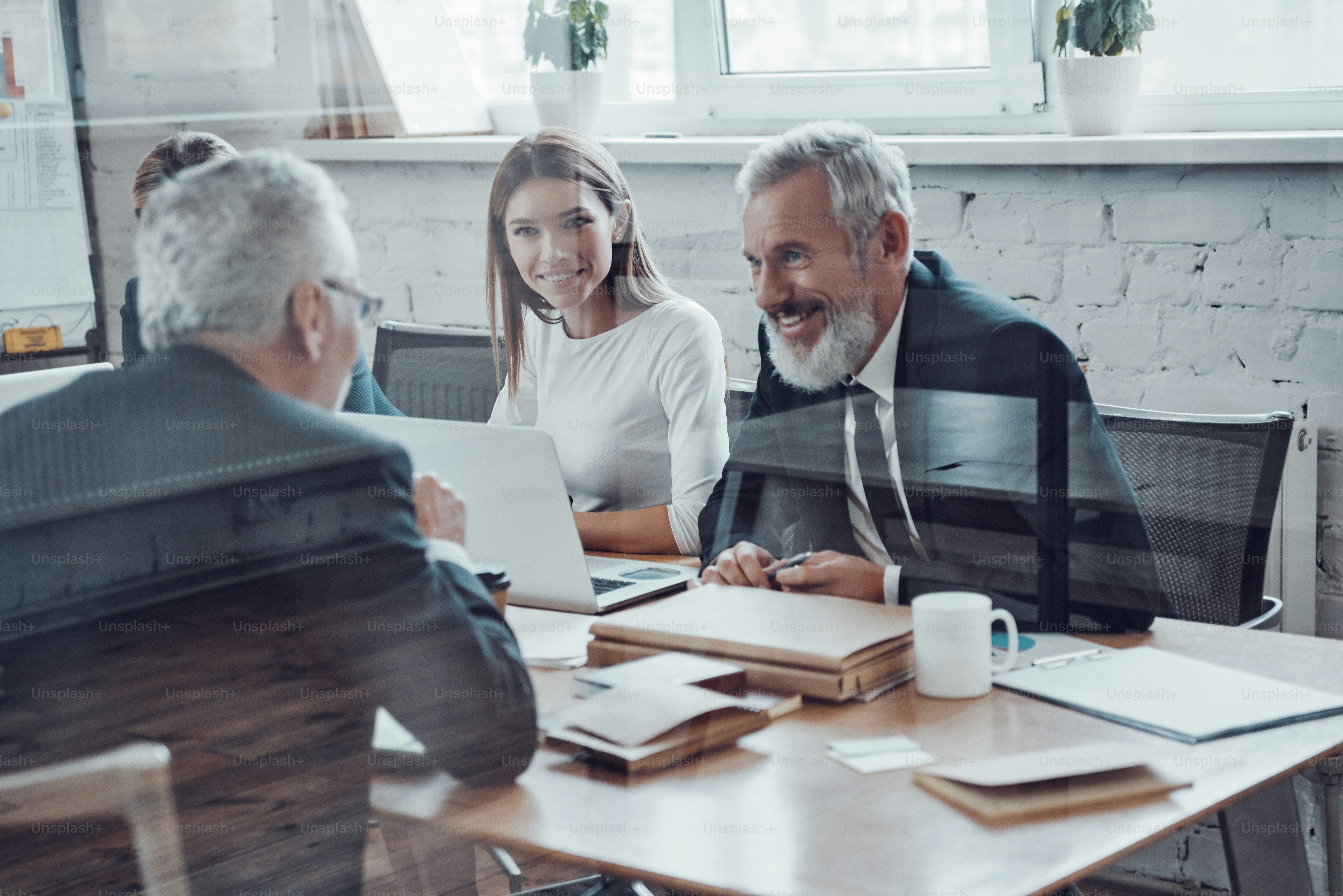 Successful business people analyzing sales using modern technologies and smiling while having staff meeting in the board room