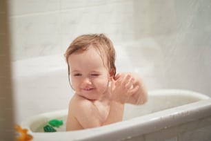 Cute little girl playing with rubber toys in small bathtub. Happy kid having fun while bathing