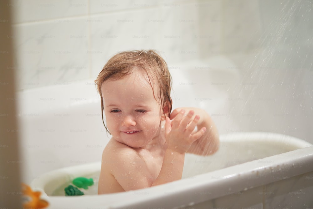 Cute little girl playing with rubber toys in small bathtub. Happy kid having fun while bathing