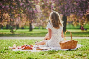 Bella giovane donna che fa picnic in una soleggiata giornata primaverile nel parco durante la stagione della fioritura dei ciliegi