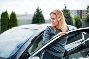 Happy young woman getting out of car in town.