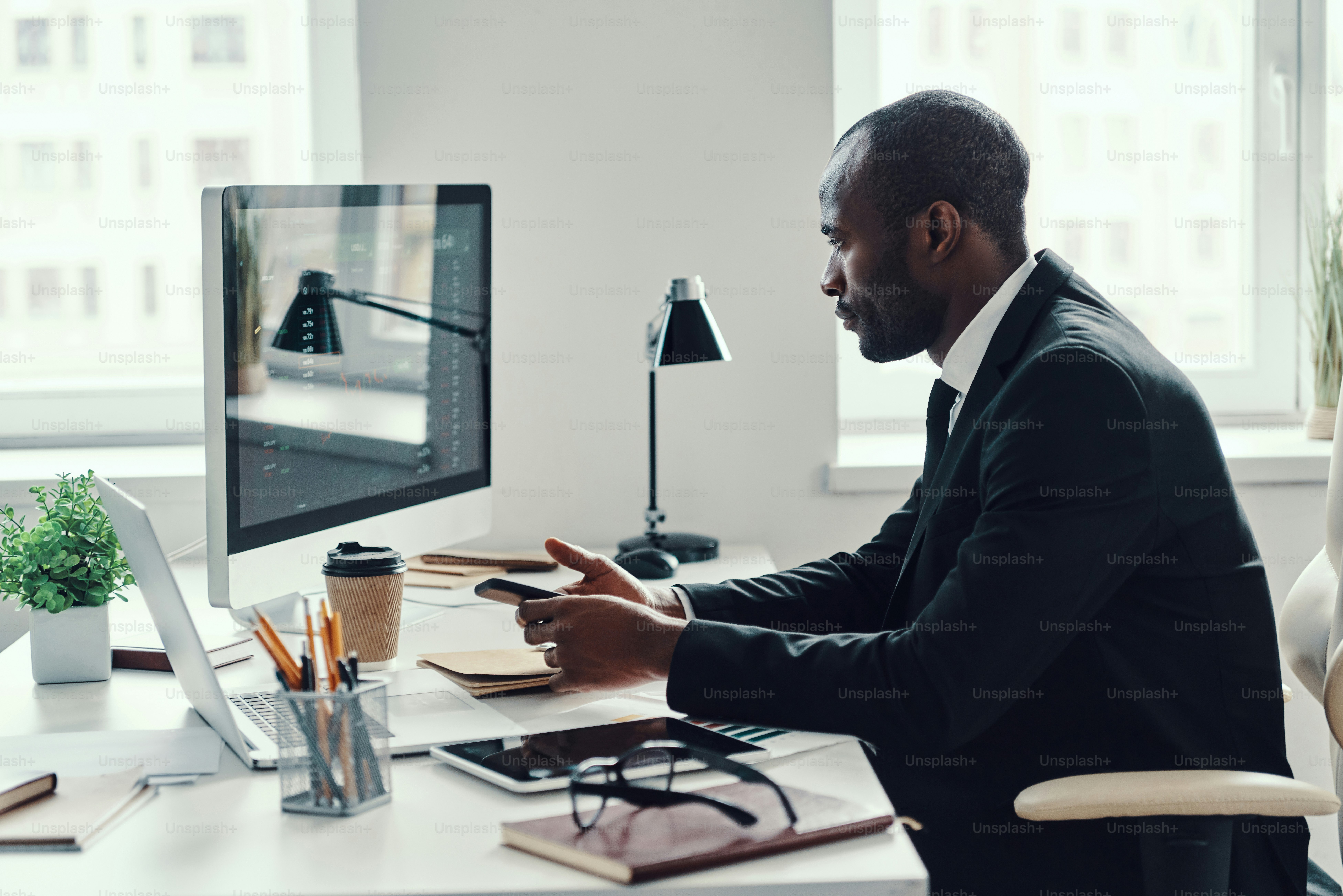 Concentrated young African man in formalwear using modern technologies while working in the office