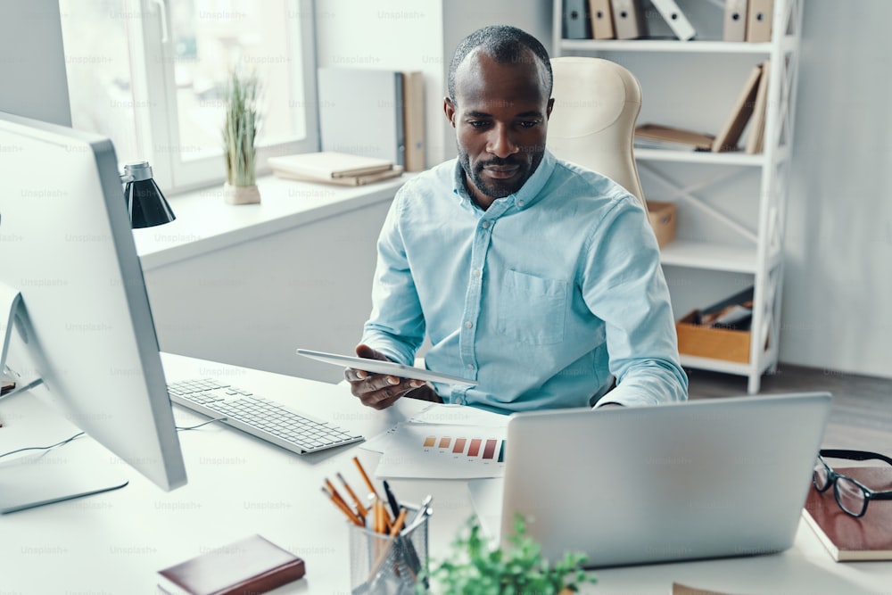 Joven africano concentrado en camisa usando tecnologías modernas mientras trabaja en la oficina