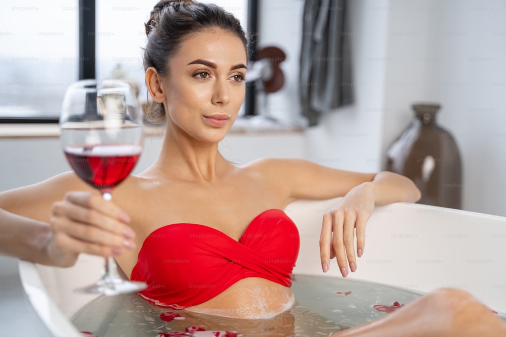 Ruhige Frau nimmt ein Bad mit einem Glas Rotwein