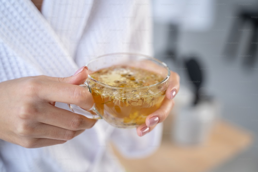 Cropped photo of female hands holding a cup of herbal beverage