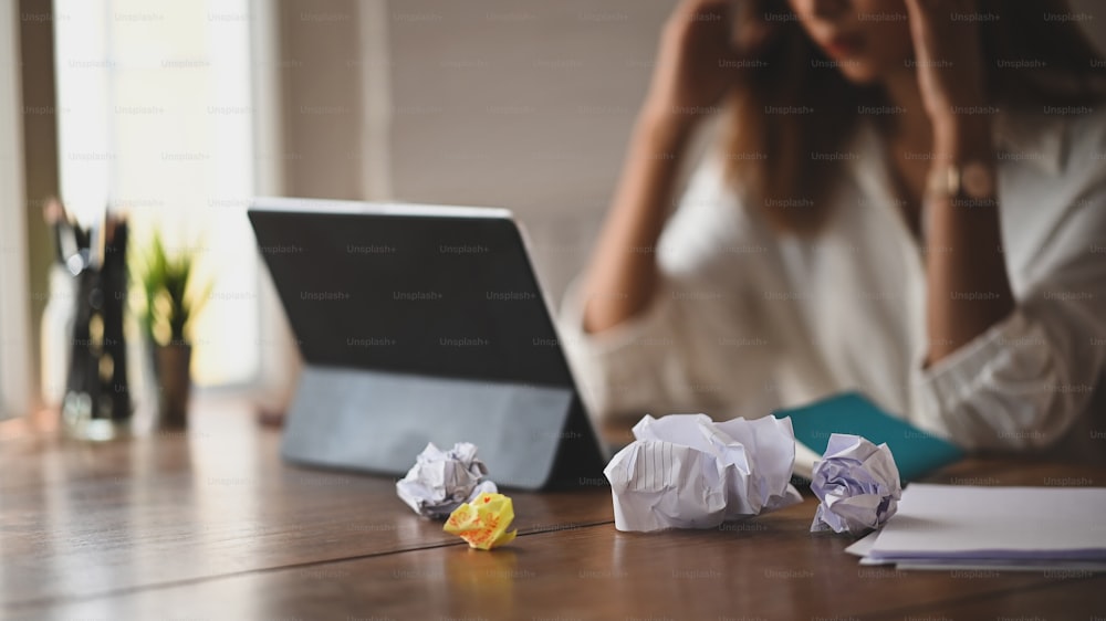 Fogli coperti accartocciati e donna seduta con la testa tra le mani alla scrivania impiegata stanca di un lavoro troppo difficile e improduttivo.