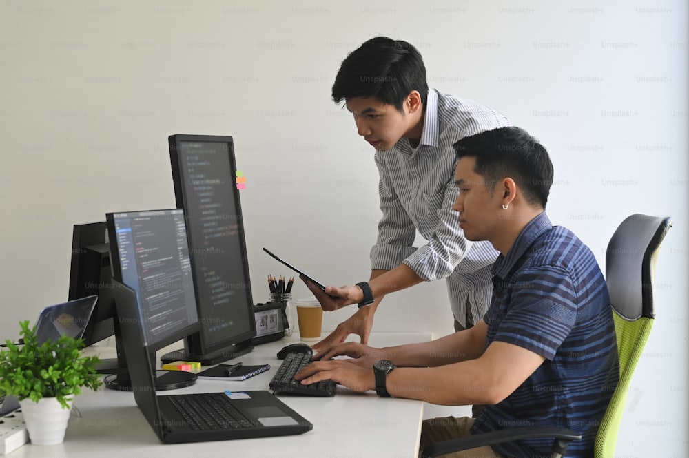 Jeunes programmeurs travaillant sur ordinateur et tablette dans un bureau moderne.