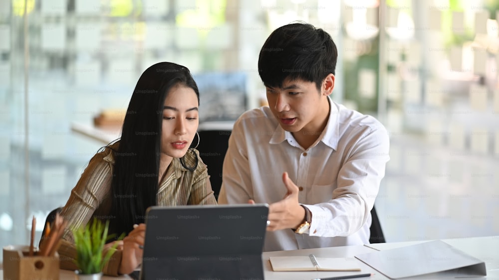 アジアのビジネスマンは、現代のオフィスでデジタルタブレットと会議をしています。