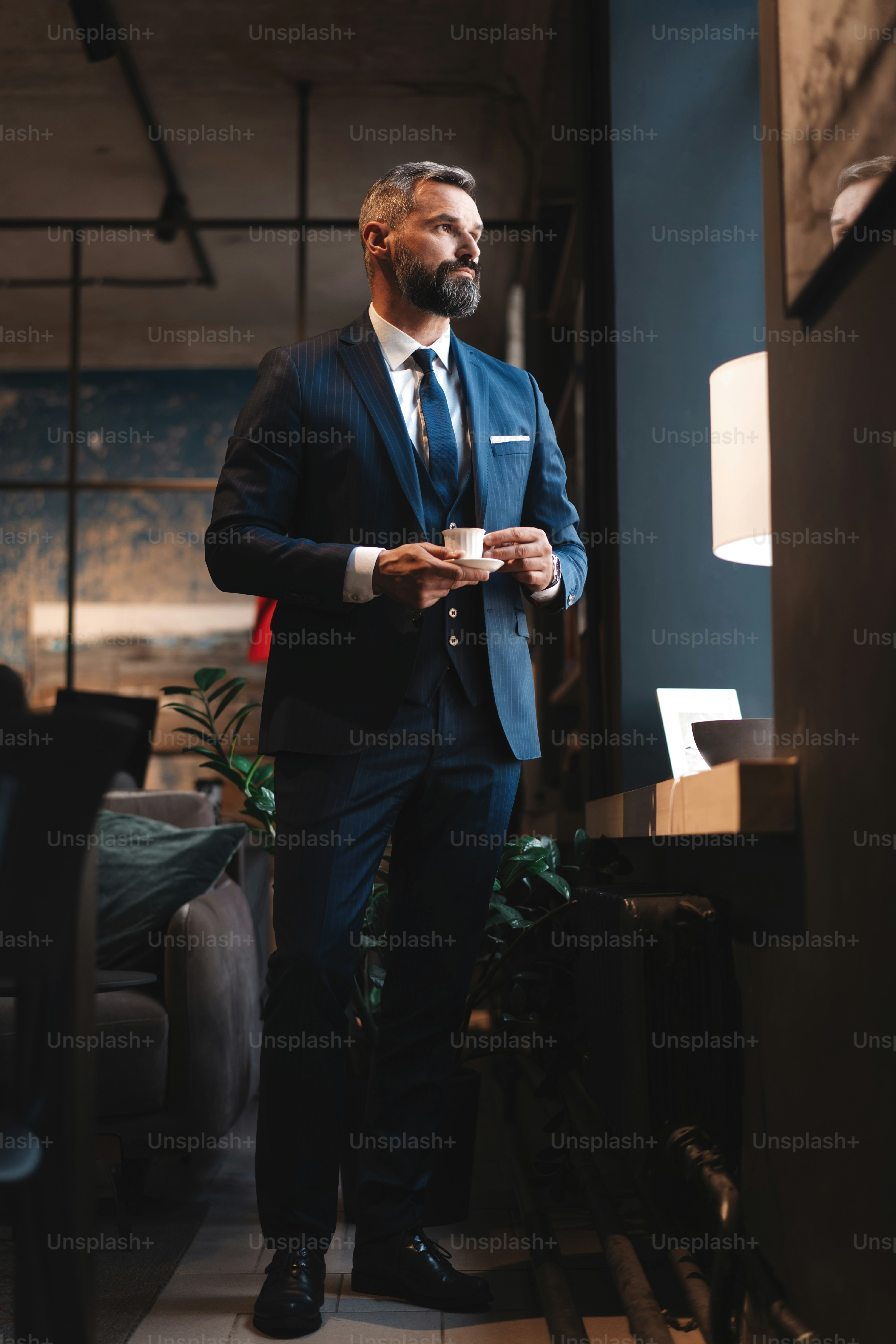 Genießen Sie frischen Kaffee während der Arbeit. Selbstbewusster Mann in schicker Freizeitkleidung mit Kaffeetasse an seinem Arbeitsplatz im Büro
