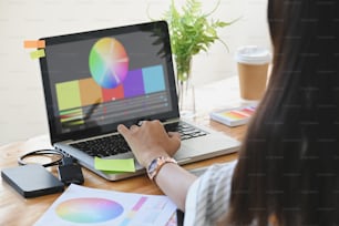 Graphic designer her selecting colour with laptop and creative accessories on table.