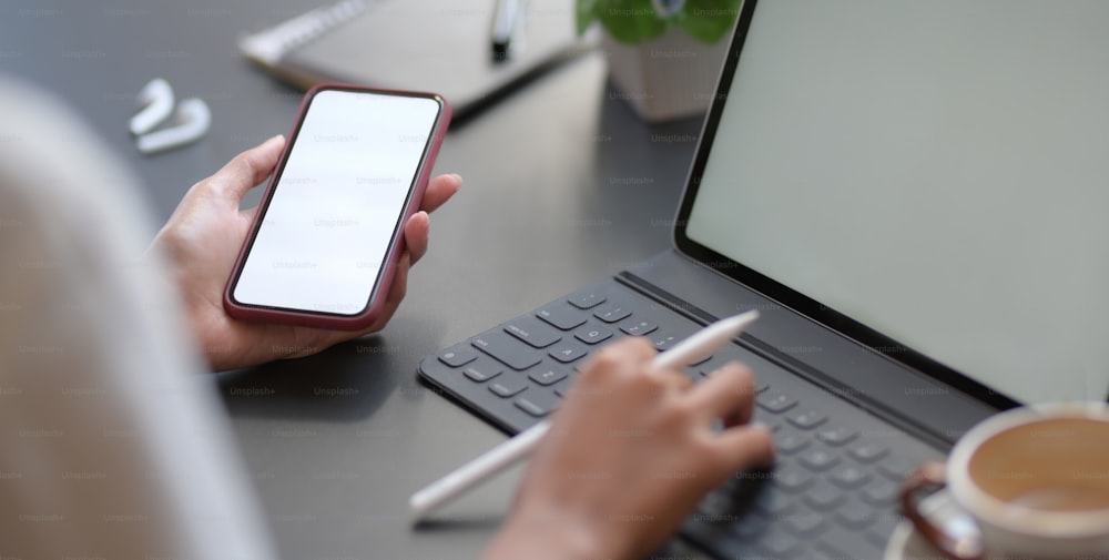 Vista de cerca de una joven empresaria que escribe en una tableta digital mientras usa un teléfono inteligente de pantalla en blanco en la sala de la oficina