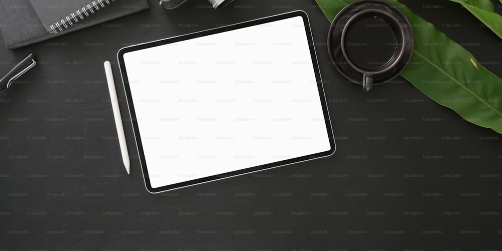 Top view of dark modern workplace with blank screen digital tablet with office supplies on black table background