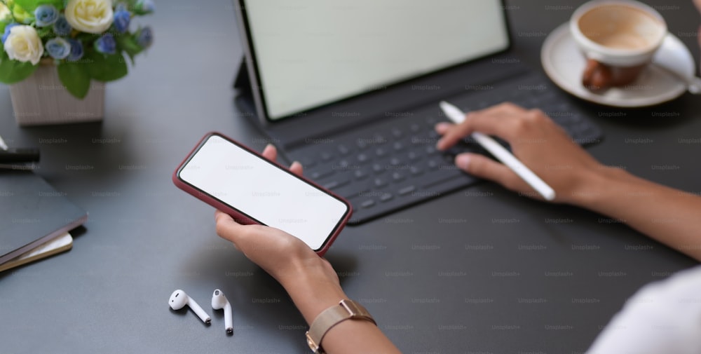 Vista de cerca de una joven empresaria que escribe en una tableta digital mientras usa un teléfono inteligente de pantalla en blanco en la sala de la oficina