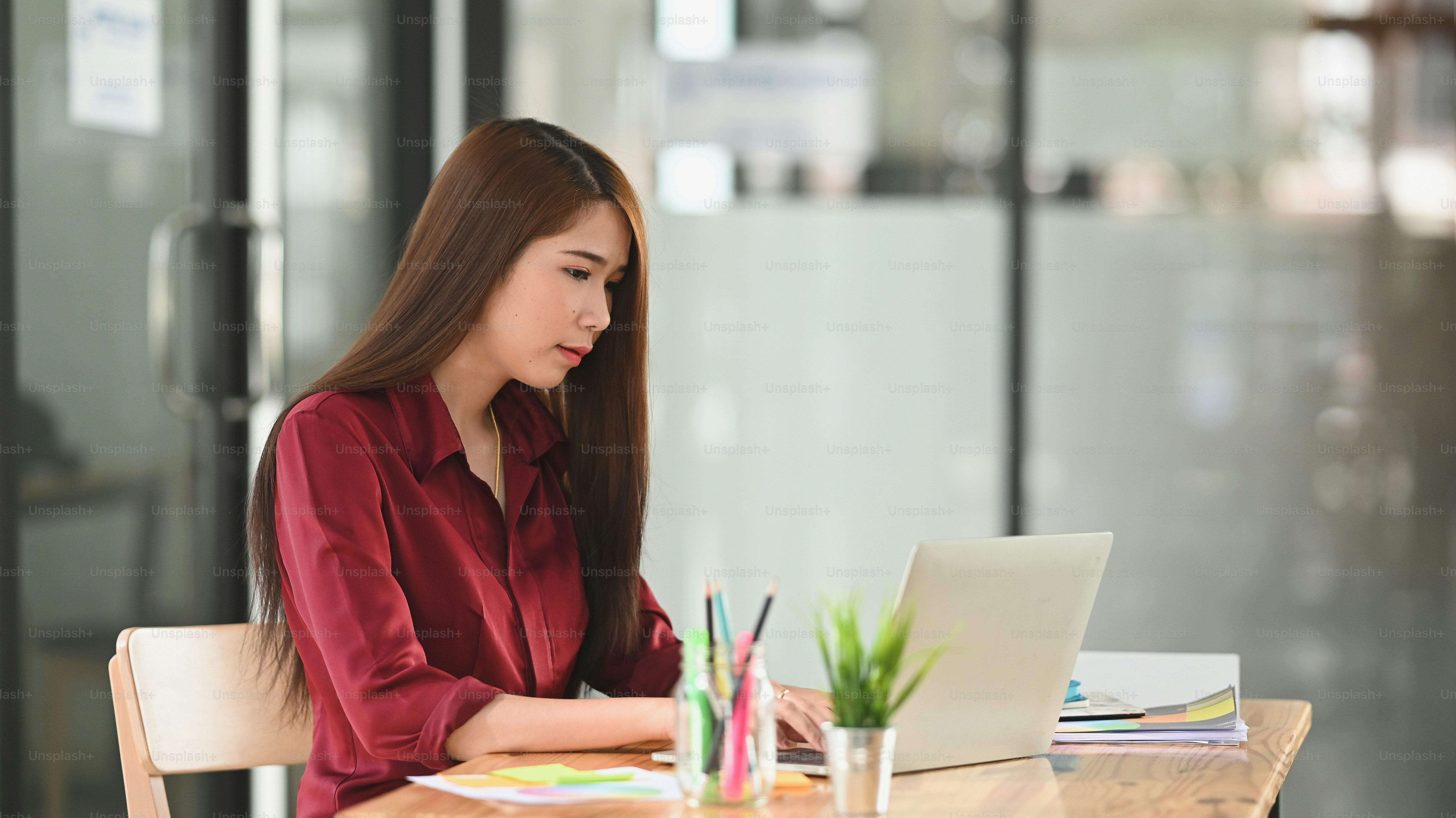 Creative young woman sitting and concentrating on work, laptop and pencil holder on the working desk.
