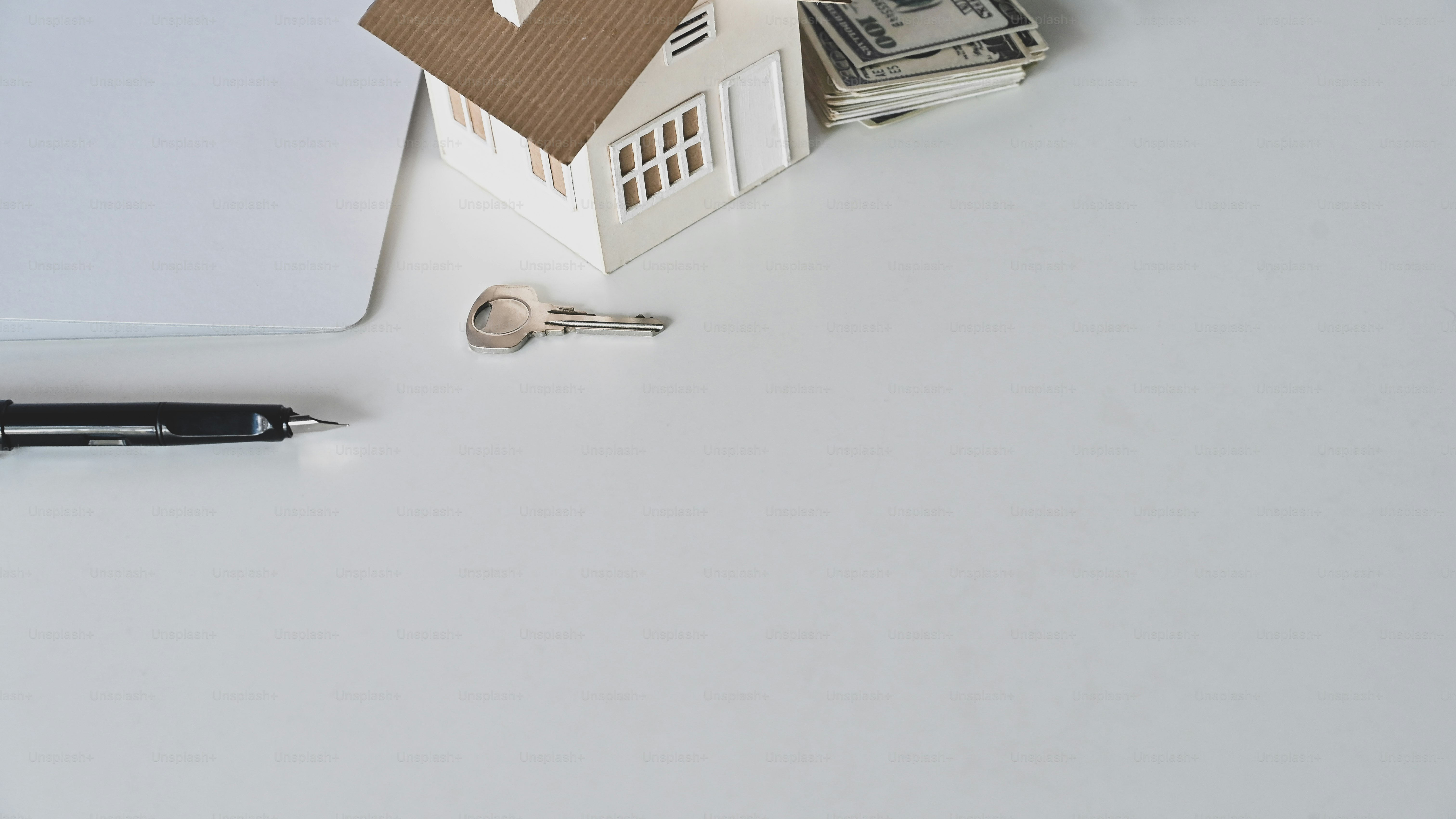 House model, rental agreement or house purchase agreement, money, paper, pen and the property's key on the white desk.