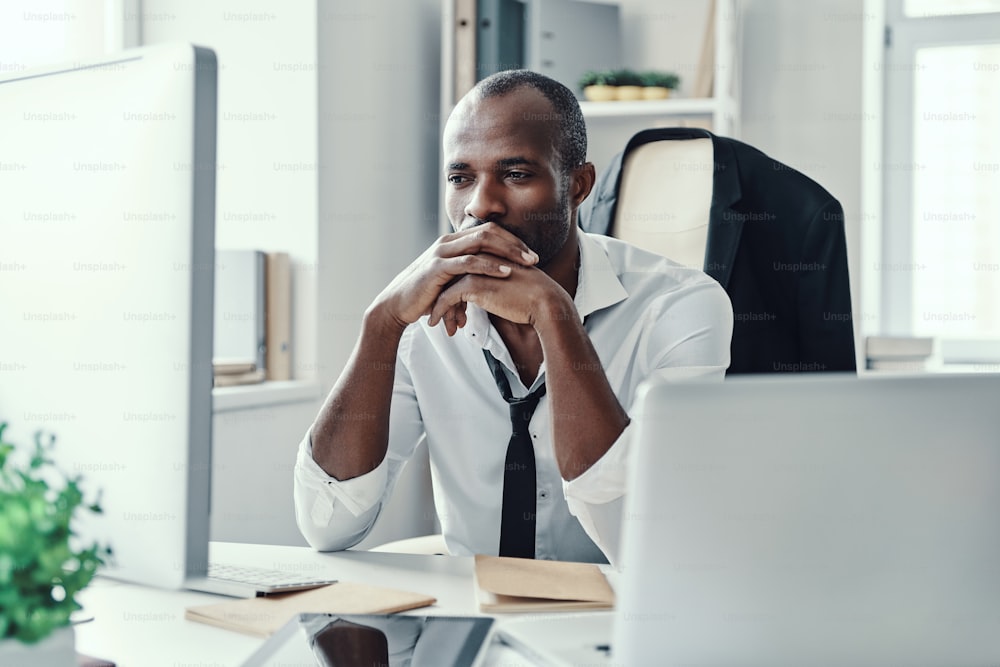 Thoughtful young African man in formalwear looking straight while working in the office